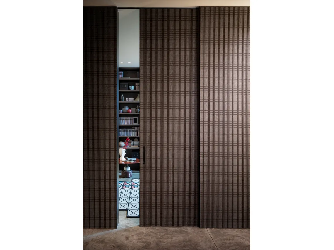 Porta per interni scorrevole con intaglio dalle geometrie tridimensionali ripetuto identico sulle pareti Chocolat di Lualdi